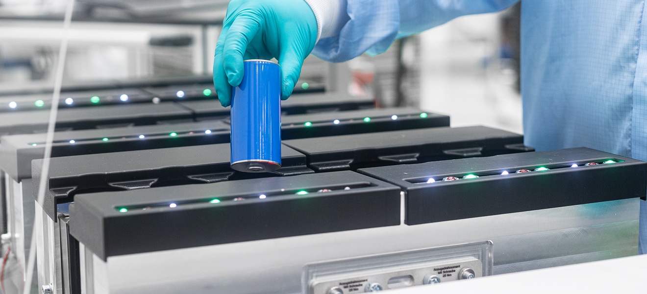 Hand mit Schutzhandschuh setzt eine Batteriezelle in die Prüfaufnahme